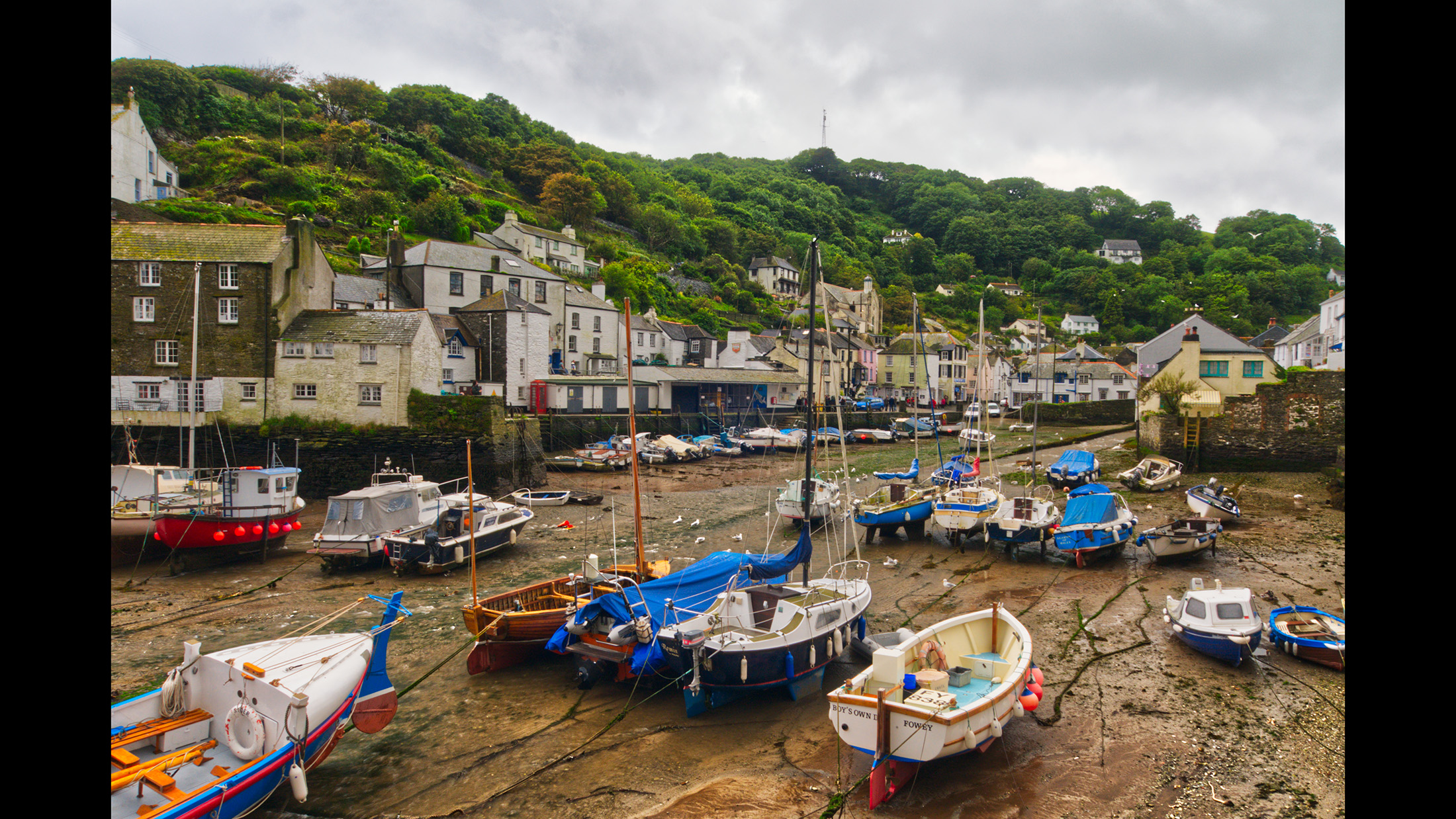Boats in a harbour with no water, cloudy sky and town