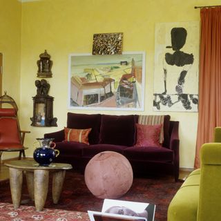 Small living room with focal point of art on the yellow painted walls with wooden furniture accents and a purple velvet two seater sofa
