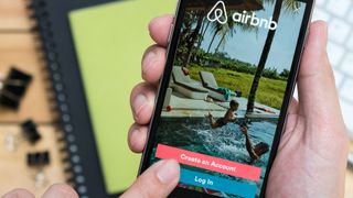 Hands holding an iPhone displaying the login page of the AirBnB app