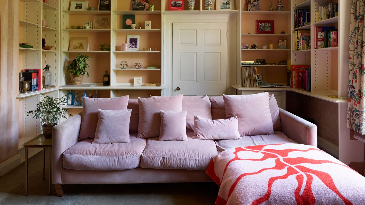 Pink chaise sofa in a beige living room with high built-in open shelves