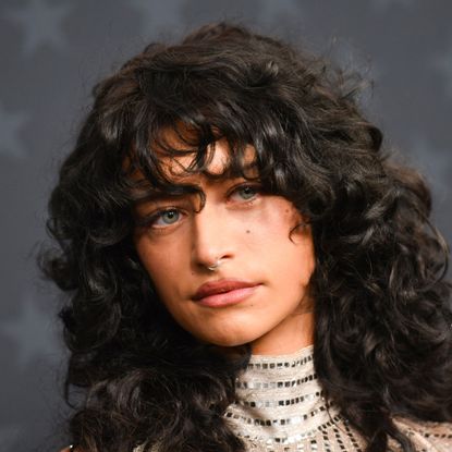 a white woman with curly black hair poses on a red carpet in front of a dark background