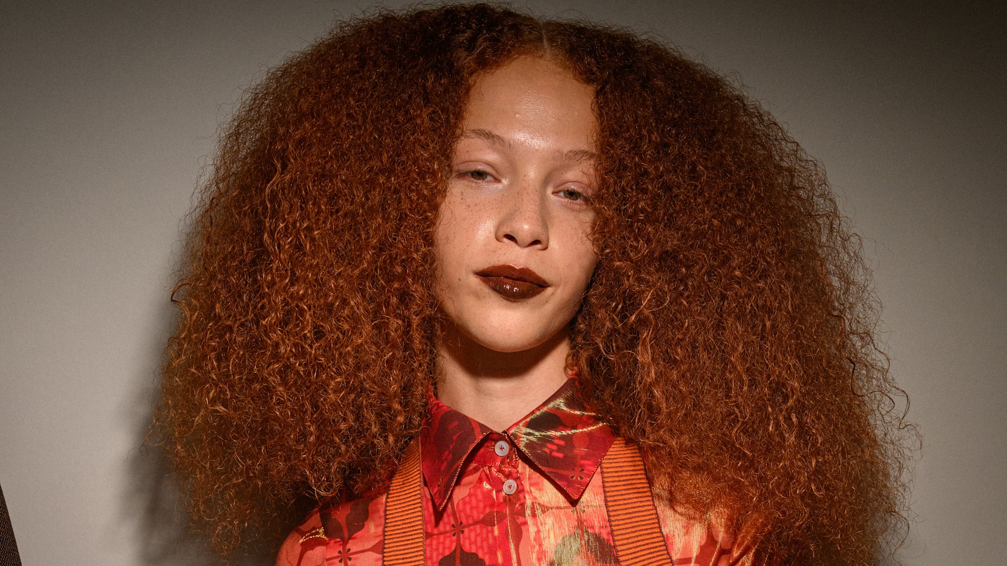 women with red curly hair in a red and orange shirt smiling at the camera