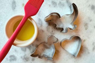 Close up of dinosaur cookie cutter with oil and a brush