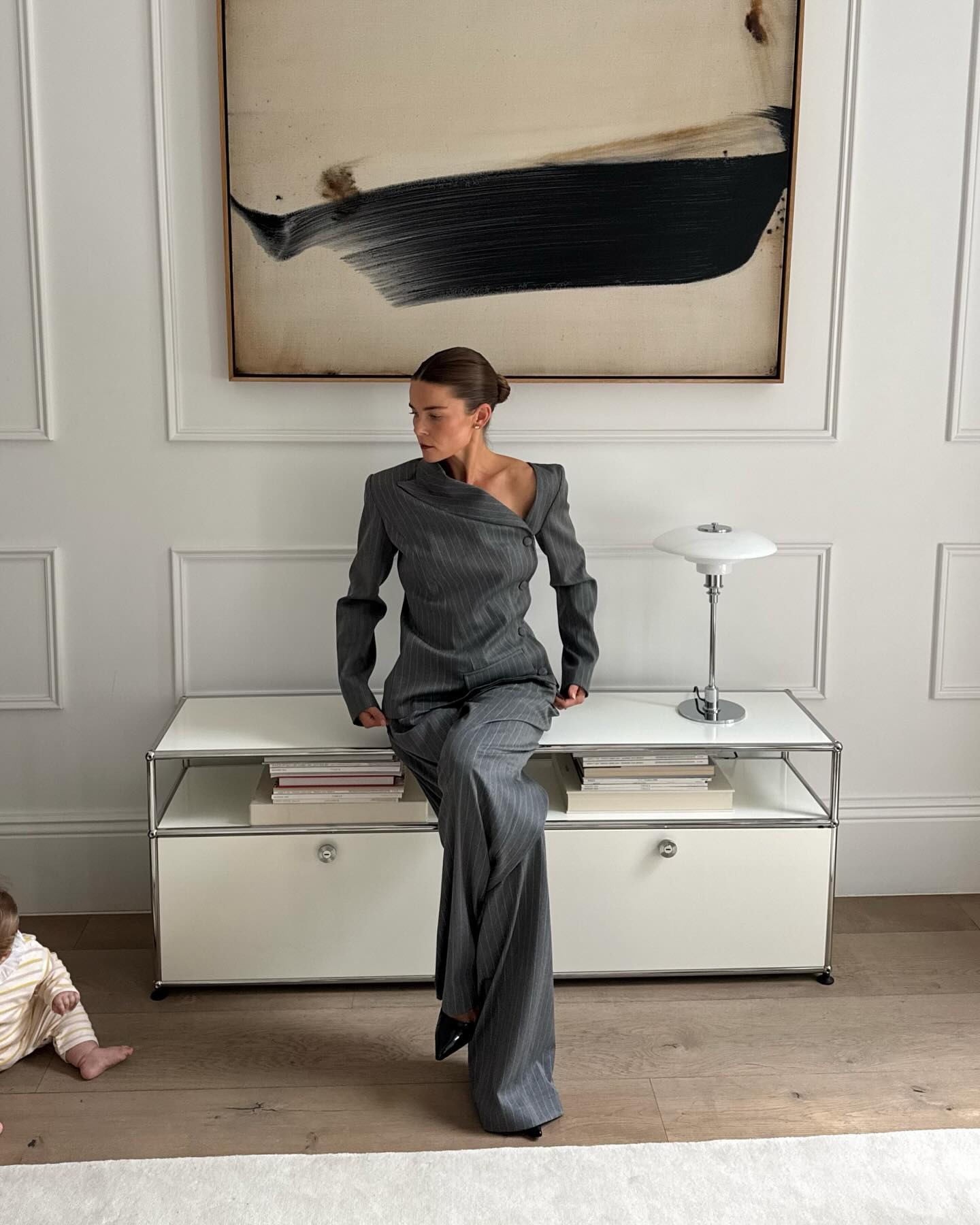 A photo of @rikkekrefting in a grey striped asymetrical suit, sitting at home