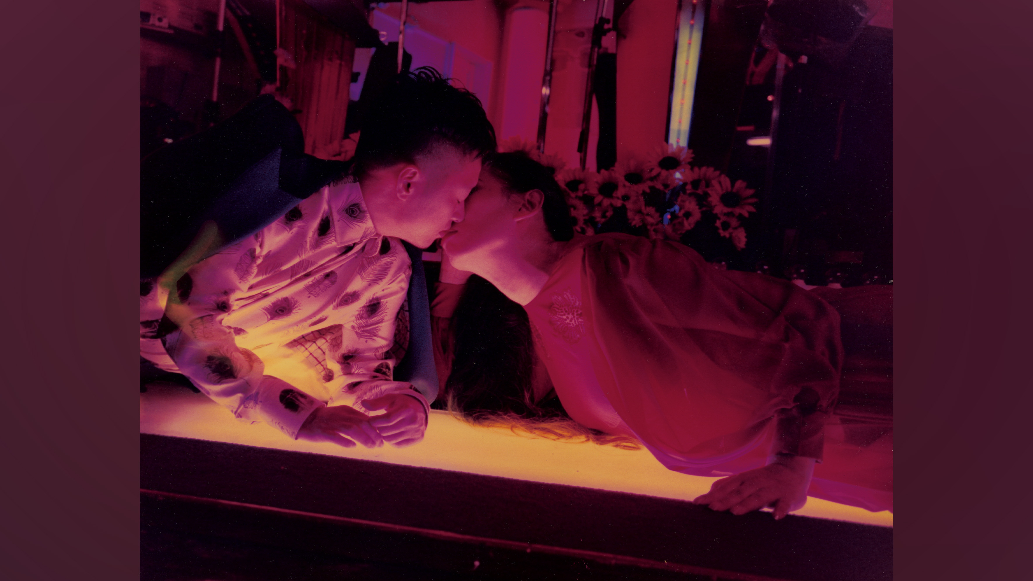 Colour photograph of two people leaning over to kiss each other.