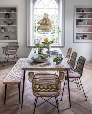 Relaxed, boho style dining room with parquet wood flooring, rattan seating, a bench and large dining table in coordinating parquet design.