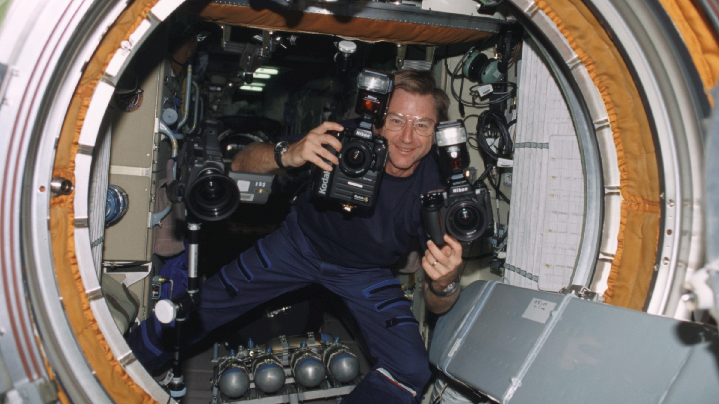 Astronaut Frank Culbertson holding two cameras while floating in zero gravity on the International Space Station in 2001