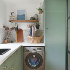 Kitchen with green cabinets, a grey washing machine, white worktop and terrazzo tiled backsplash