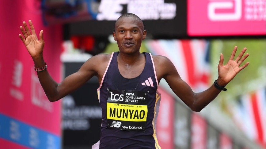 Alex Mutiso, wearing black running gear, raises his arms in the air after winning a long-distance race.