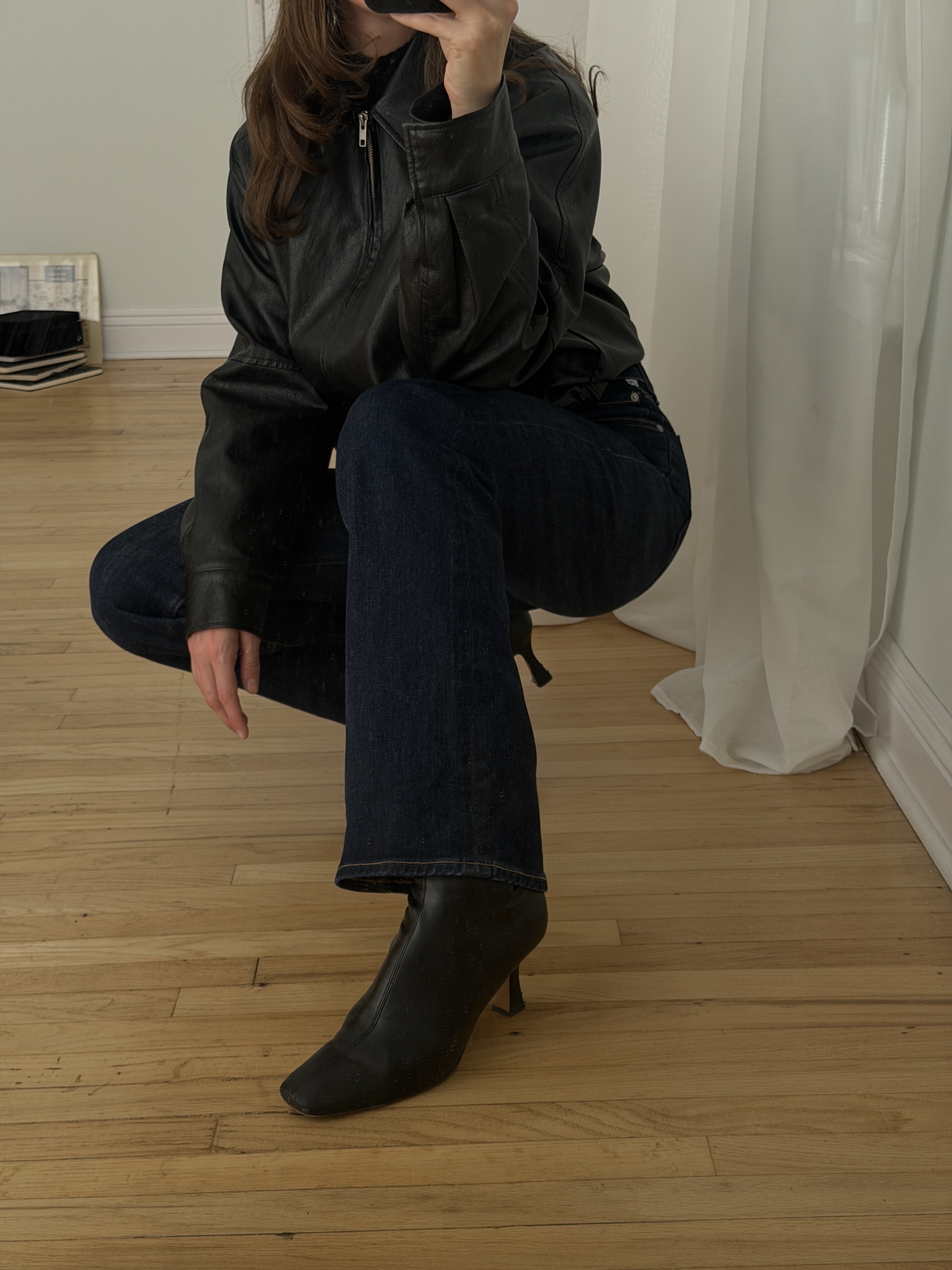 Kathryn Zahorak posing in mirror wearing leather jacket, dark wash jeans, and black boots