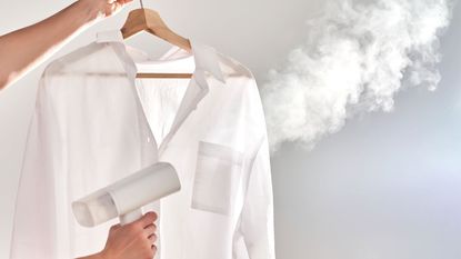 Someone holding up a white shirt and steaming it with a handheld steamer 
