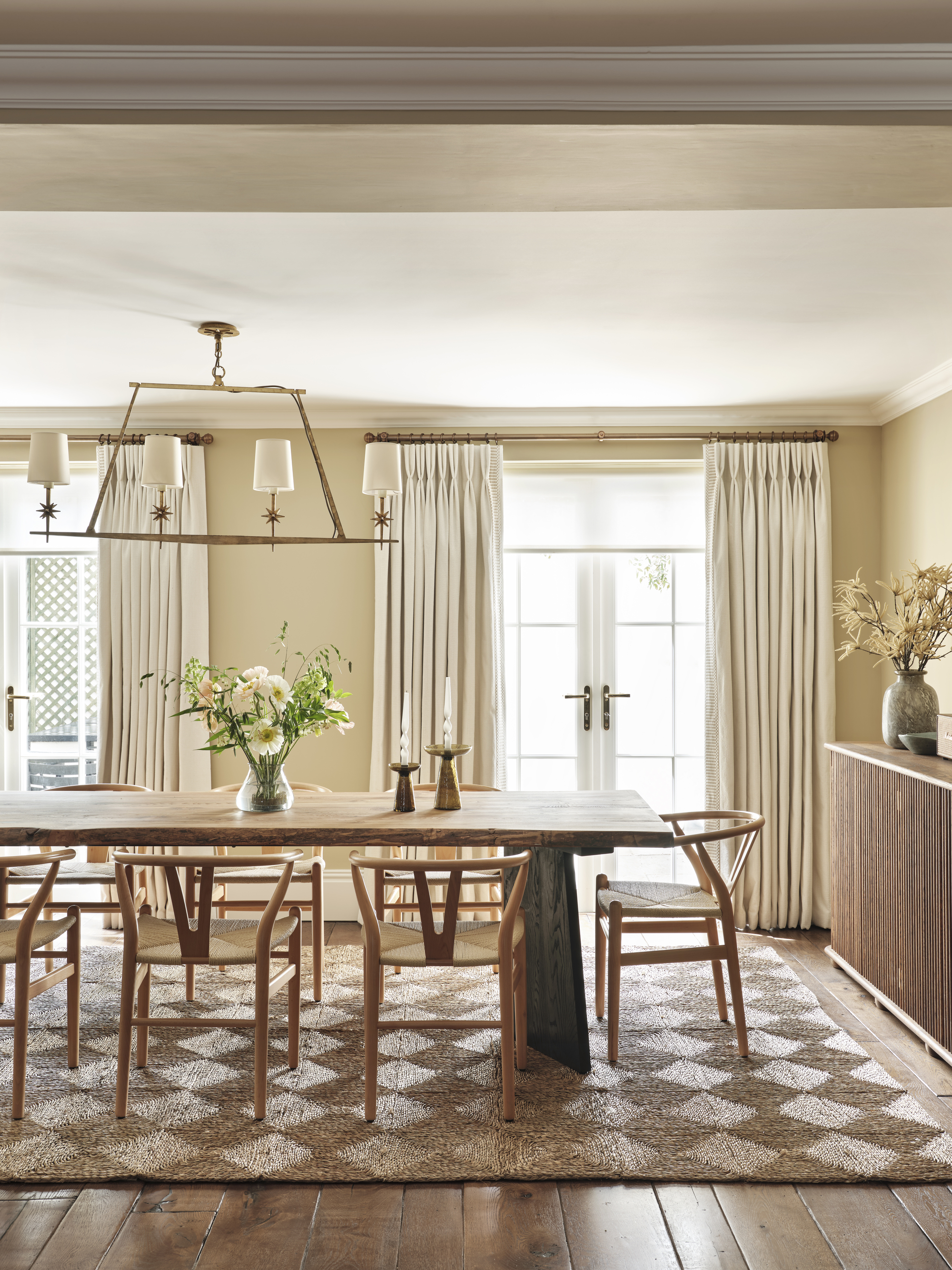 A dining room with a natural woven seagrass rug, a large wooden dining table, and a neutral color palette