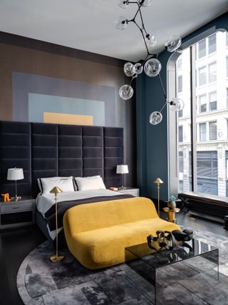 Bedroom with velvet headboard, yellow sofa and abstract light fixture