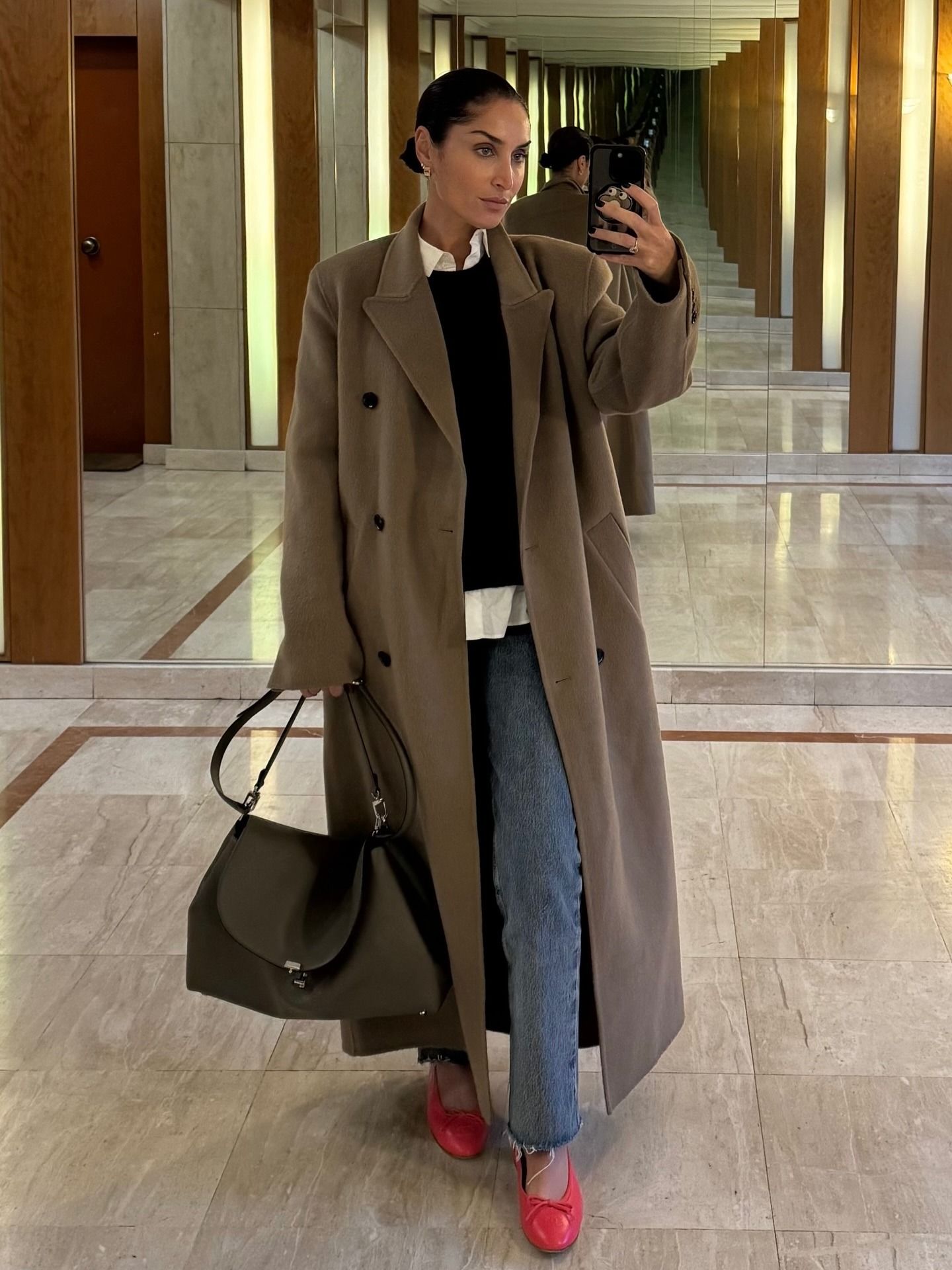 Erin wears a beige coat, black sweater, sim straight jeans, red ballet flats.