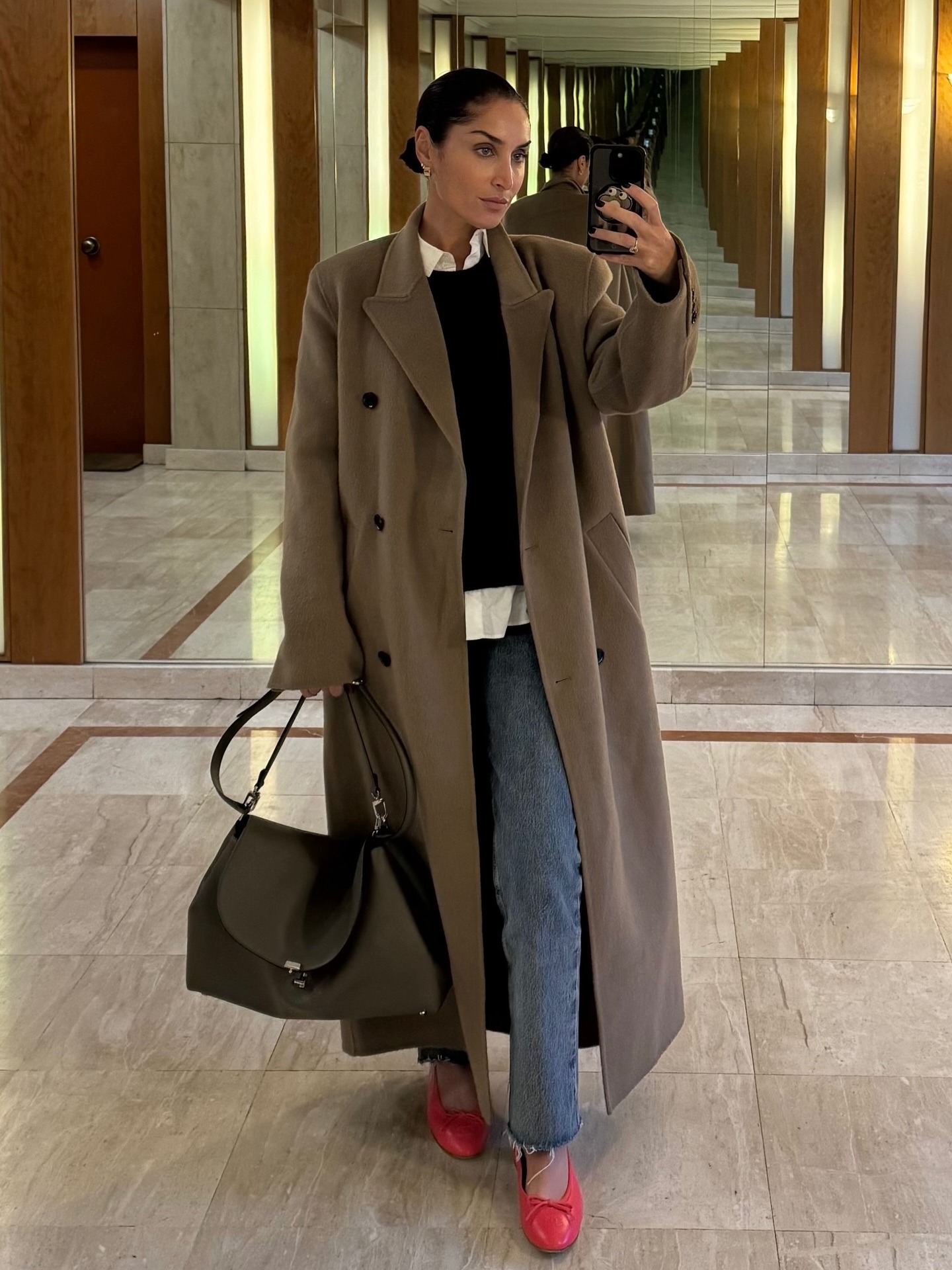 Erin wears a beige coat, black sweater, sim straight jeans, red ballet flats.