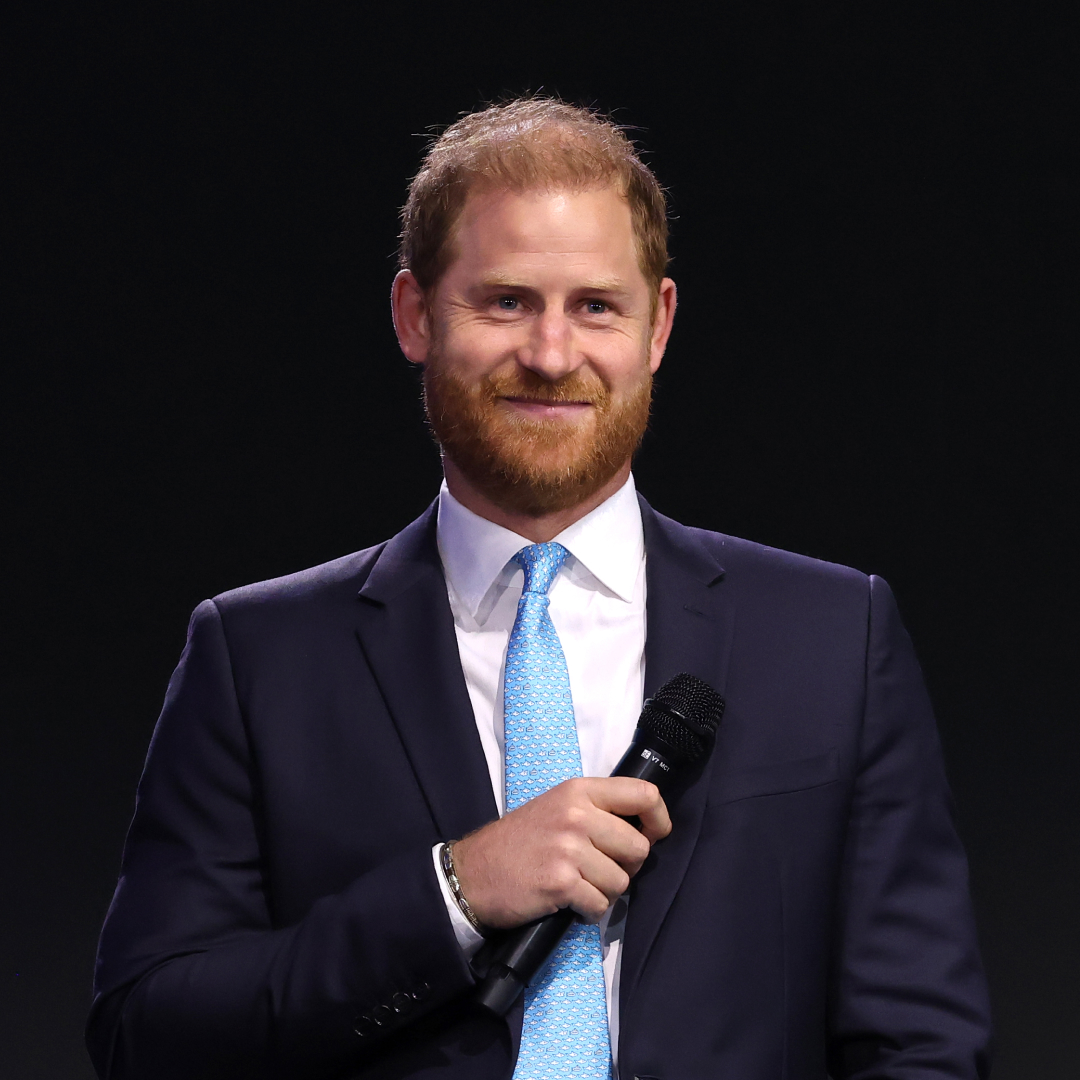 Prince Harry wears a suit with a baby blue tie and white shirt and has red