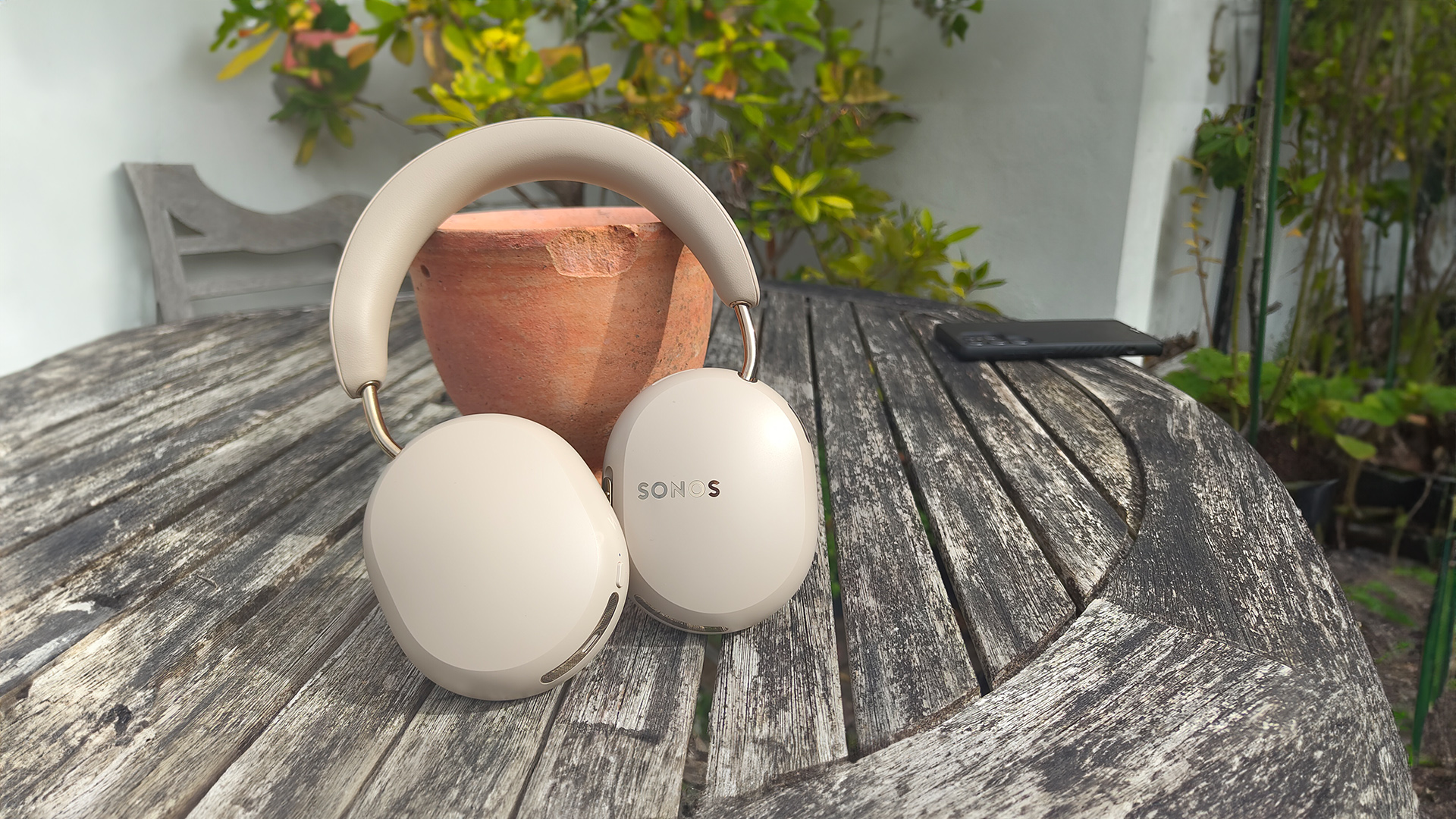 Sonos Ace Ultra wireless headphones on wooden outdoor table leaning against plant pot