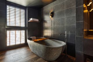Macq 01 hotel bathroom with oval granite bath, grey wall tiles and brown floor tiles