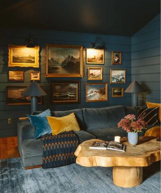 Vintage art frames on wood panelled wool in snug room with velvet sofa and wooden coffee table