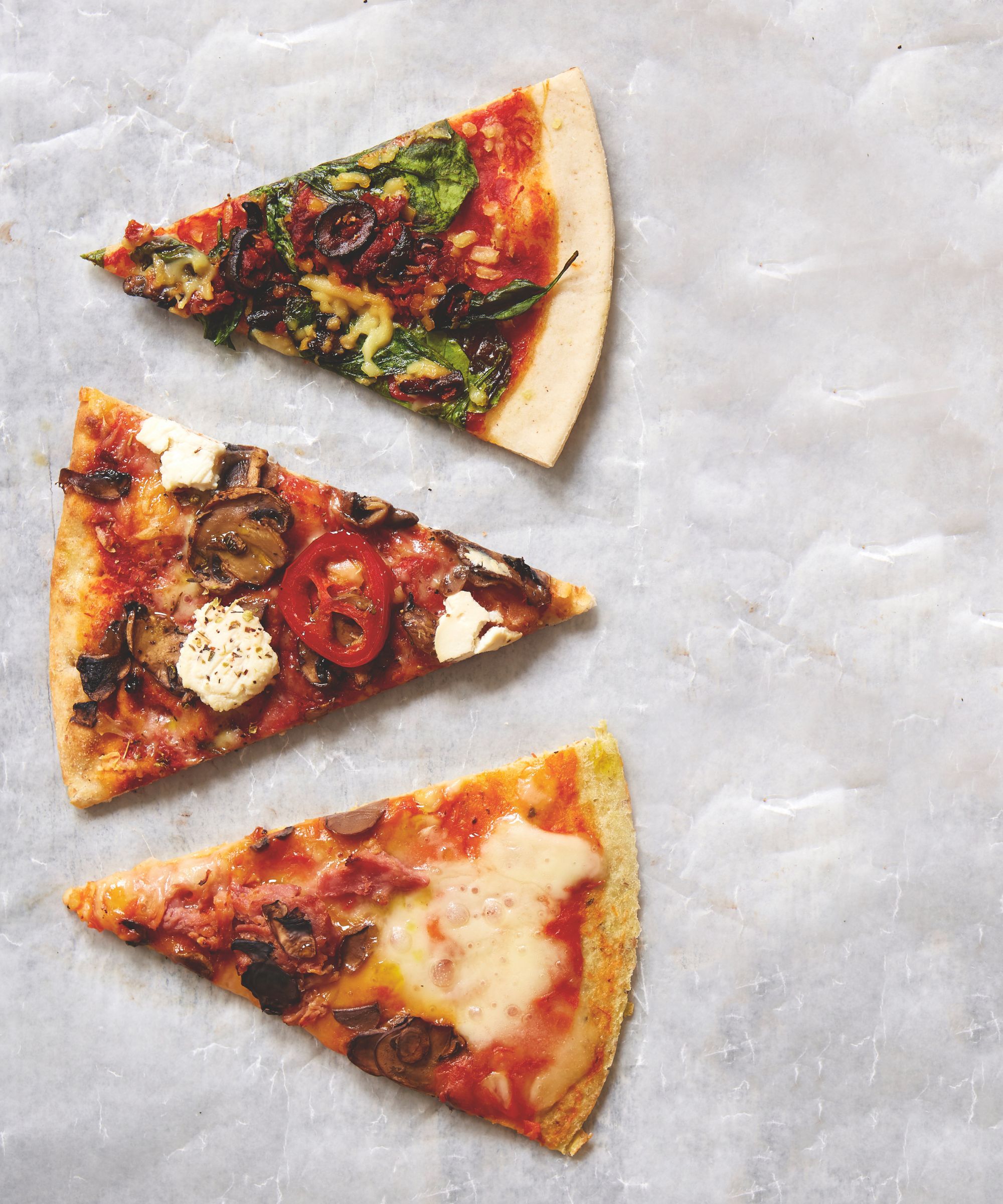 three slices of different pizza on a white marble surface
