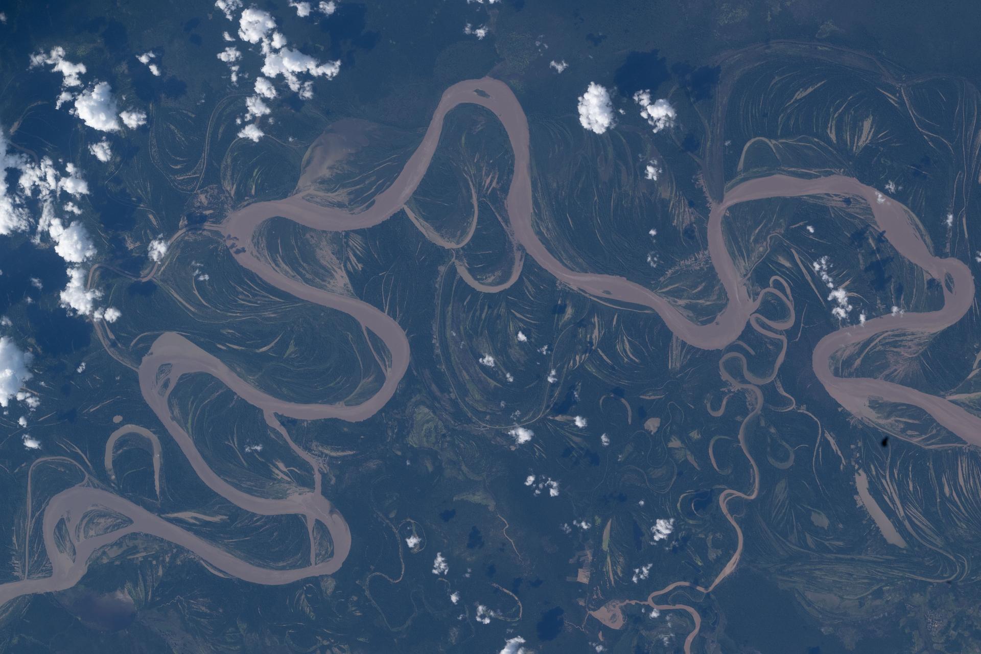 An image of the Ucayali River taken from space shows the river snaking in a light brown color across dark blue and green land with some small fluffy white clouds overhead.