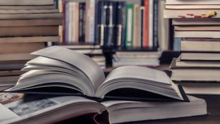 A background of books on shelves and an open book on a table in the foreground