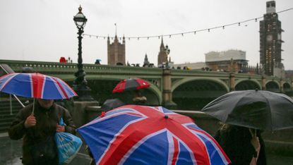Pedestrians shelter from the rain beneath Union flag-themed umbrellas