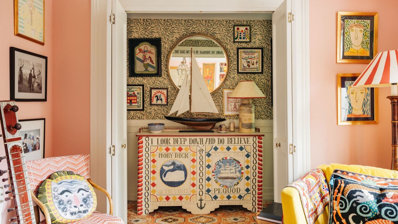 Folk style living room with painted cabinet, printed wallpaper, embroidered cushions and pink walls