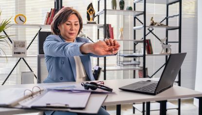 Businesswoman sitting at desk stretching her wrist