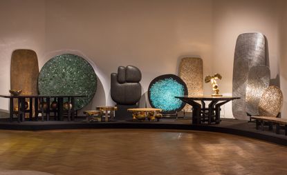 Ado Chale’s experimental furniture inspired by mineralogy is now on view at Bozar in Brussels. A variety of different tables and decorations on a raised platform.