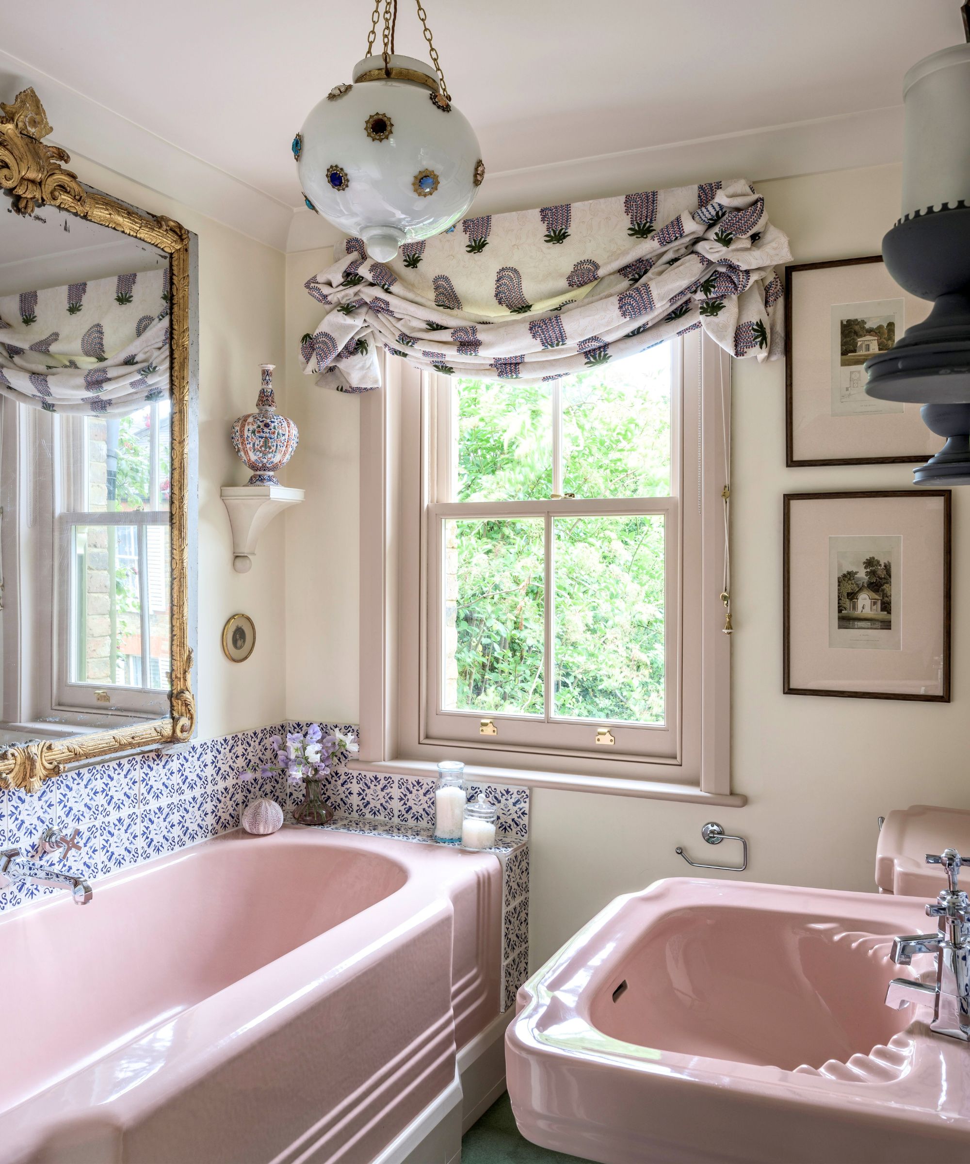 Bathroom with pink tub and sink, green carpet, ornate gold mirror, roman blind, vintage glass pendant light and blue and white tiles