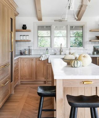 checklist for modern rustic style, kitchen with wood cabinets and floor, white marble countertops, black stools, pumpkins on island, beams, open plan shelving