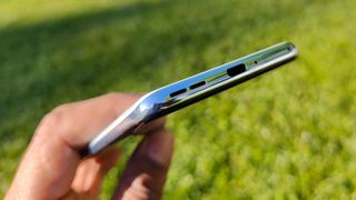 En hånd holder OnePlus Nord 2T, så vi kan se bunden - med en græsplæne i baggrunden