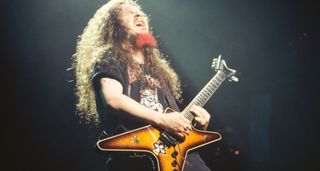 Dimebag Darrell of Pantera grimaces as he takes a solo on his sunburst Dean ML electric guitar. His goatee is dyed bright red.