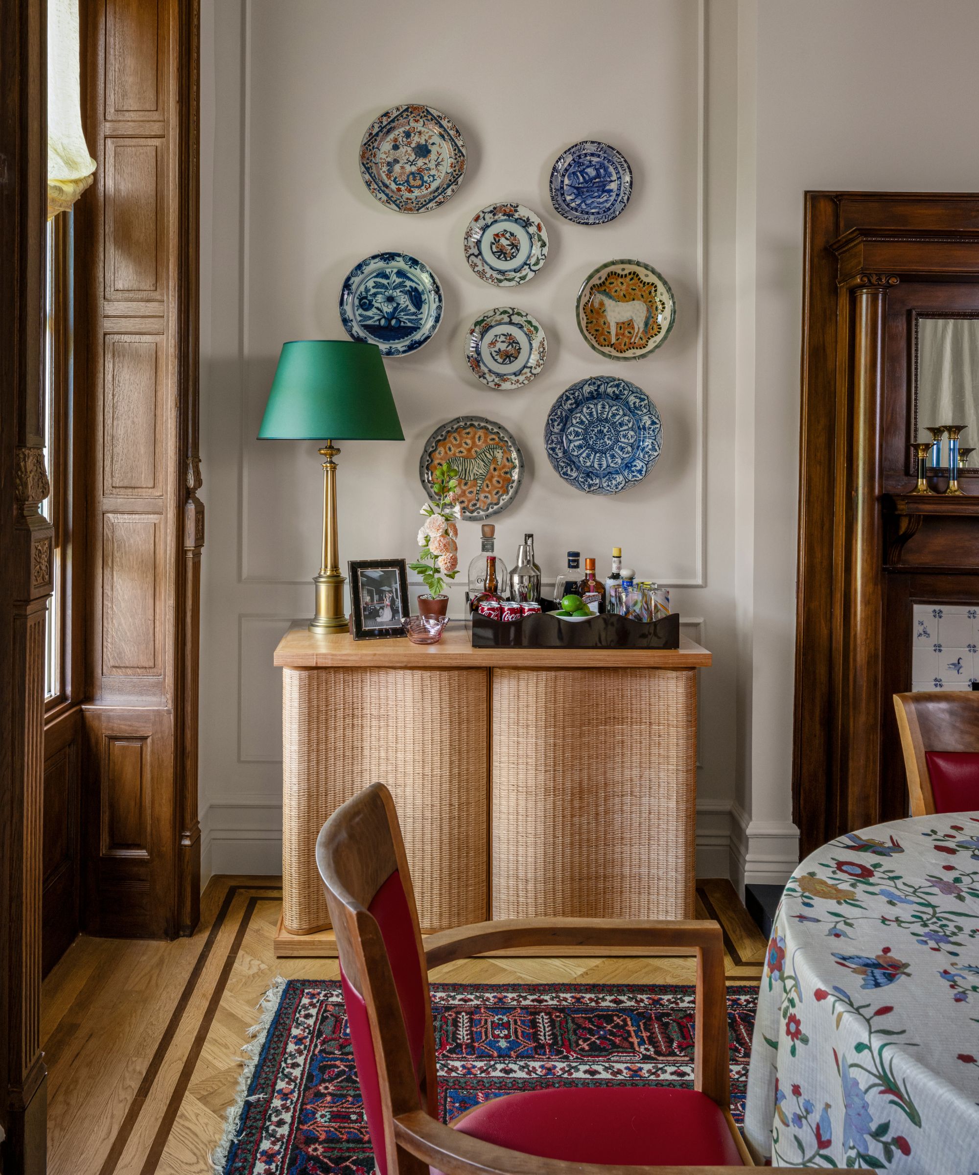 a neutral dining room in a historic brownstone with wooden fireplace, original windows, and a wicker console styled with antique plates
