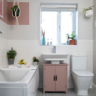 white bathroom with pink colour blocking pink vanity unit white suite macrame plant hanger