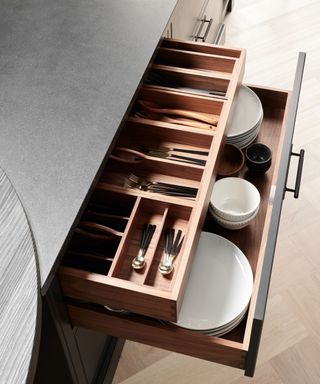 A black kitchen counter with open drawers with kitchen utensils and white plates inside it