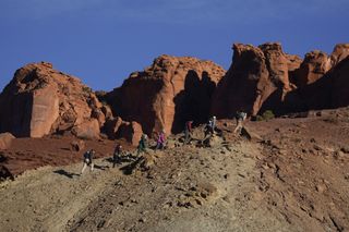 a group of hikers near a large rock formation against a blue sky.