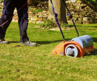 person using a lawn scarifier to remove lawn moss and debris