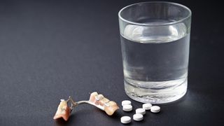 Denture tablets and false teeth next to a glass of water