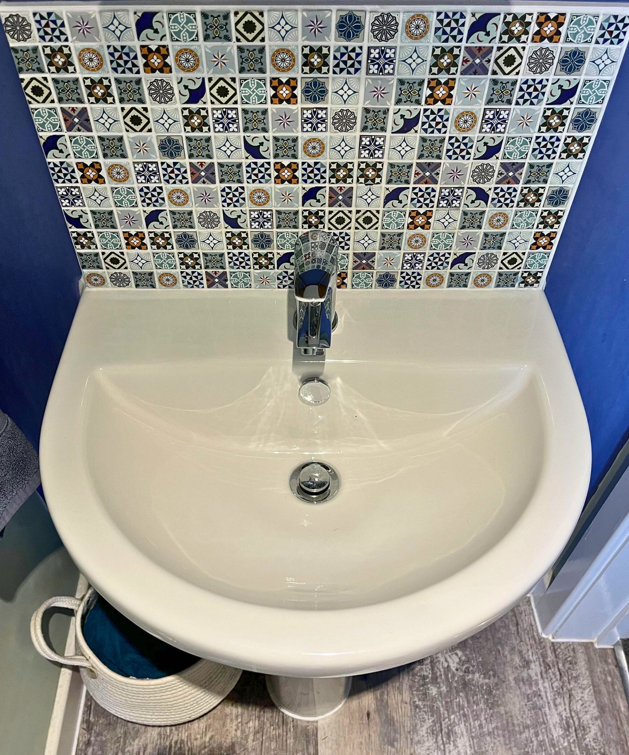 Clean white bathroom sink with mosaic backsplash, chrome mixer tap and blue wall paint