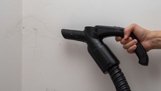 Vacuuming cobwebs off a plain white wall
