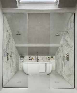 An example of master bathroom ideas showing a walk-in shower with marble paneled walls, a freestanding white tub and glass shower panels
