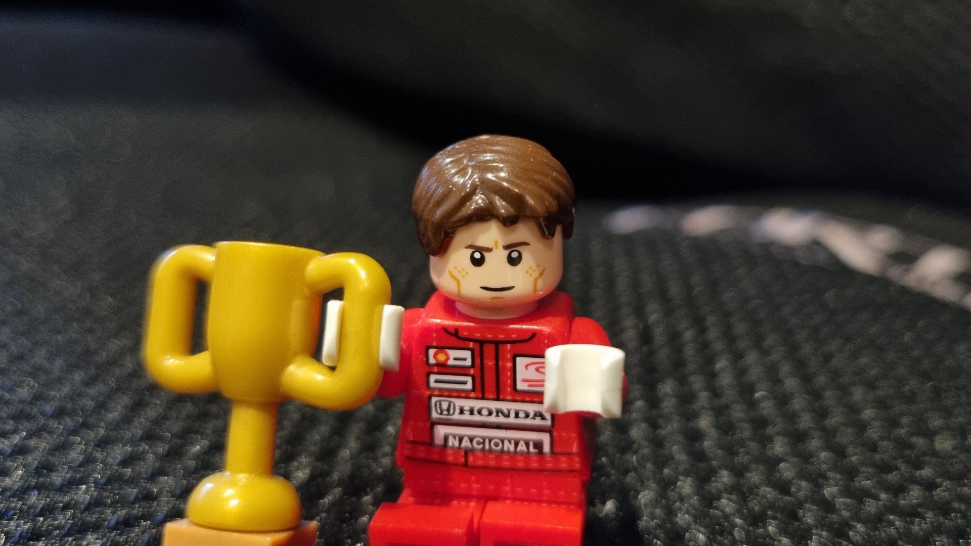 A Lego minifig Ayrton Senna looking annoyed on a gaming chair cushion.