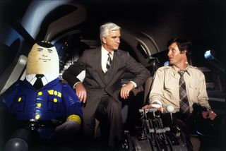 Dr. Rumack (Leslie Nielsen) speaks to Ted Striker (Robert Hays) as he steers the plane next to an inflatable pilot in Airplane!