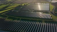 An aerial of a solar farm with hundreds of solar panels on green fields