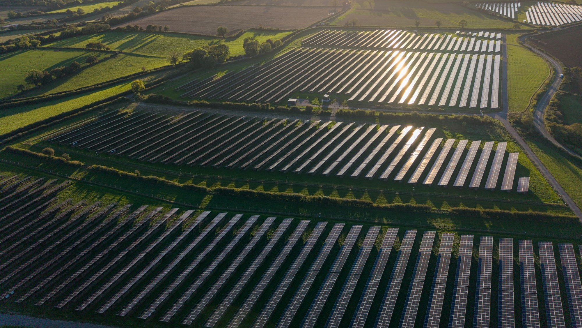 An aerial of a solar farm with hundreds of solar panels on green fields