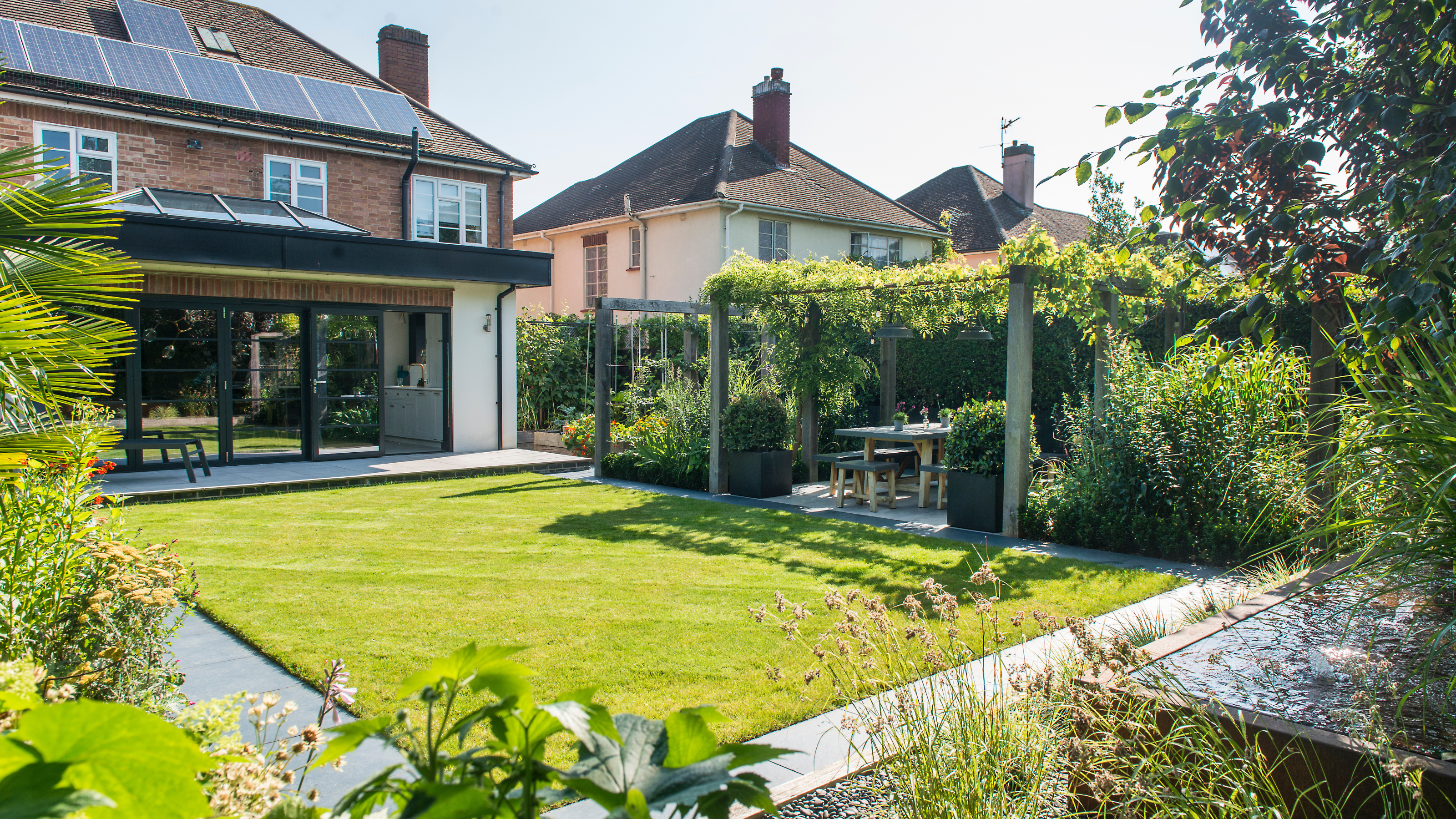A neat, green lawn bordered by a pergola and flower beds.