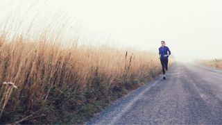 Woman running along pavement through fields in activewear, grey skies