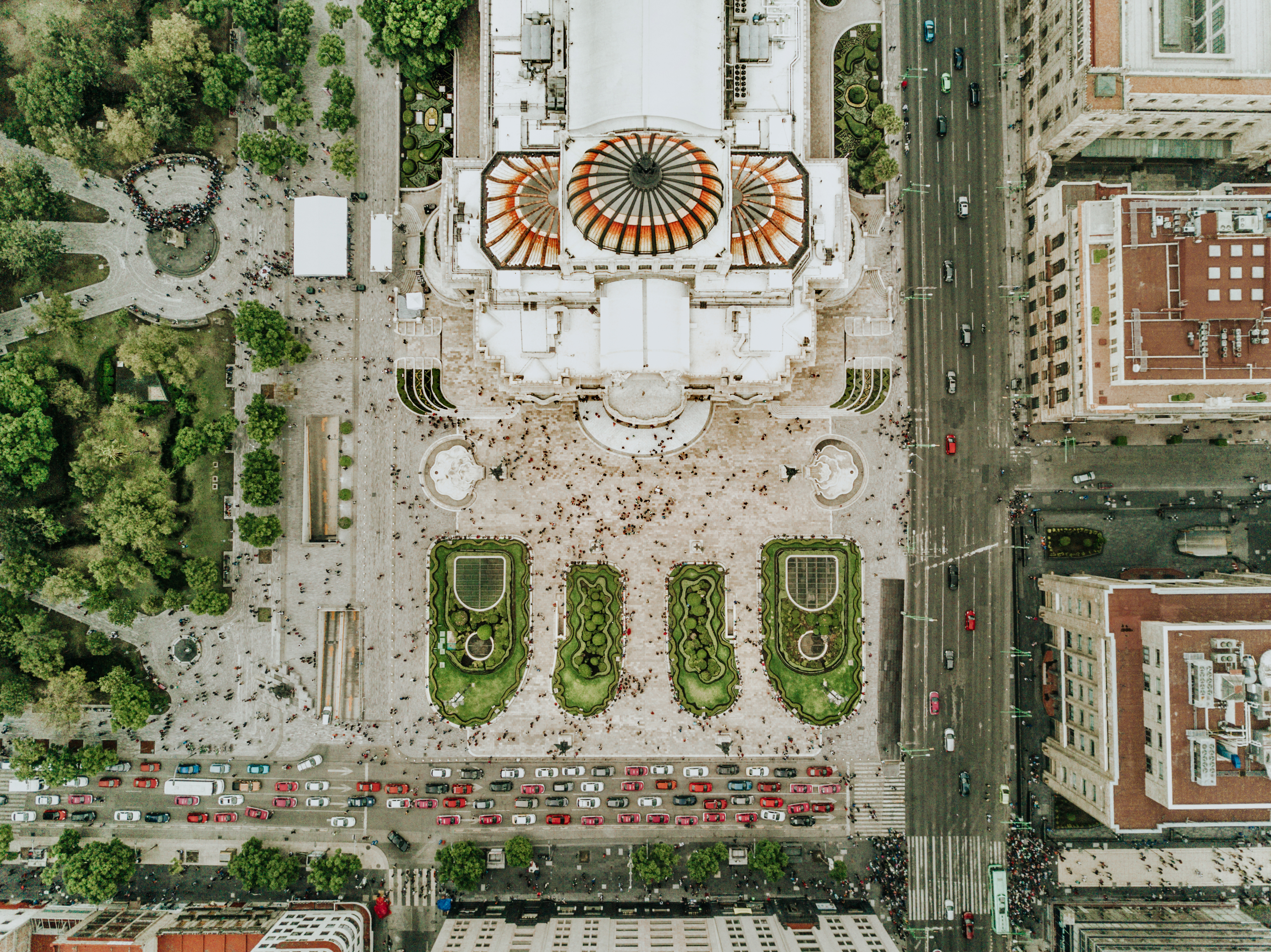 An aerial view of a crowded Mexican square with a striking white, red, and black temple and lots of pockets of greenery.